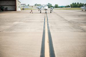 Student walking toward at Delta State plane that's sitting on the runway next to the hanger.