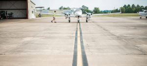 Student walking toward at Delta State plane that's sitting on the runway next to the hanger.