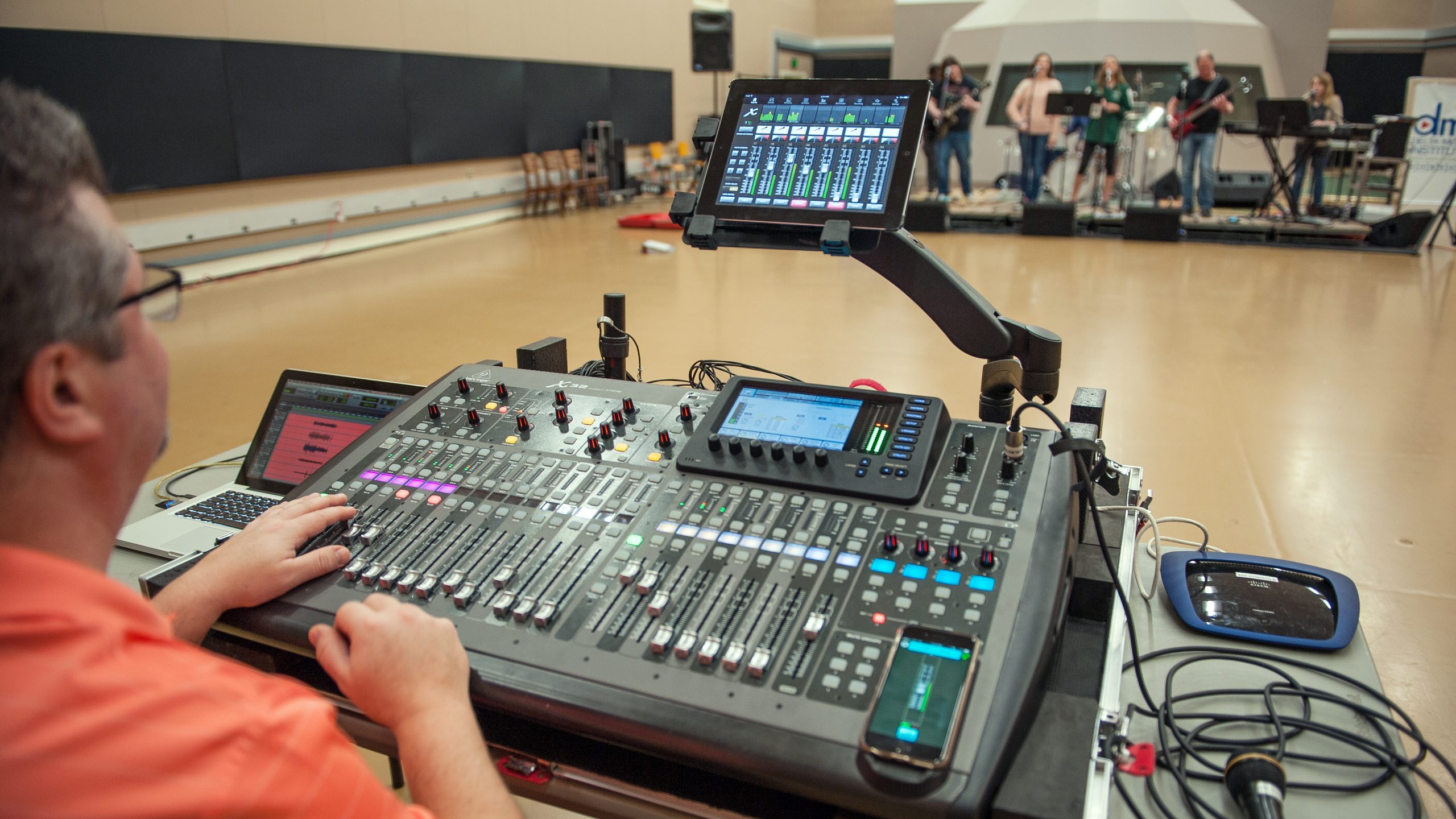 Man controlling digital sound board for a 6-piece band performing on a stage.