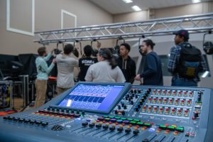 Seven students setting up live sound equipment and lighting with a digital console in front, already powered on.