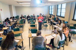 Students surrounding professor in a classroom setting while professor is teaching.