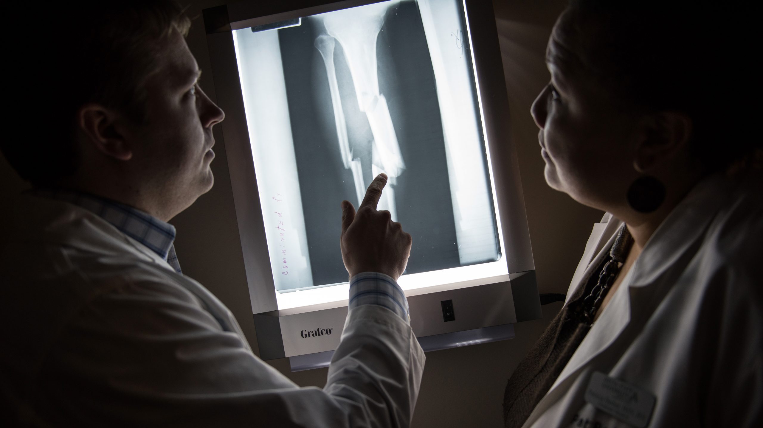 Two nursing students interpreting x-ray of broken bone in a dark room.