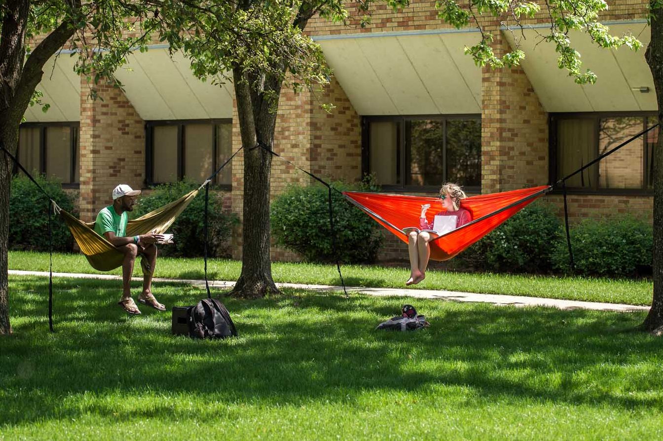 Two students on campus, relaxing in hammocks during summer school.