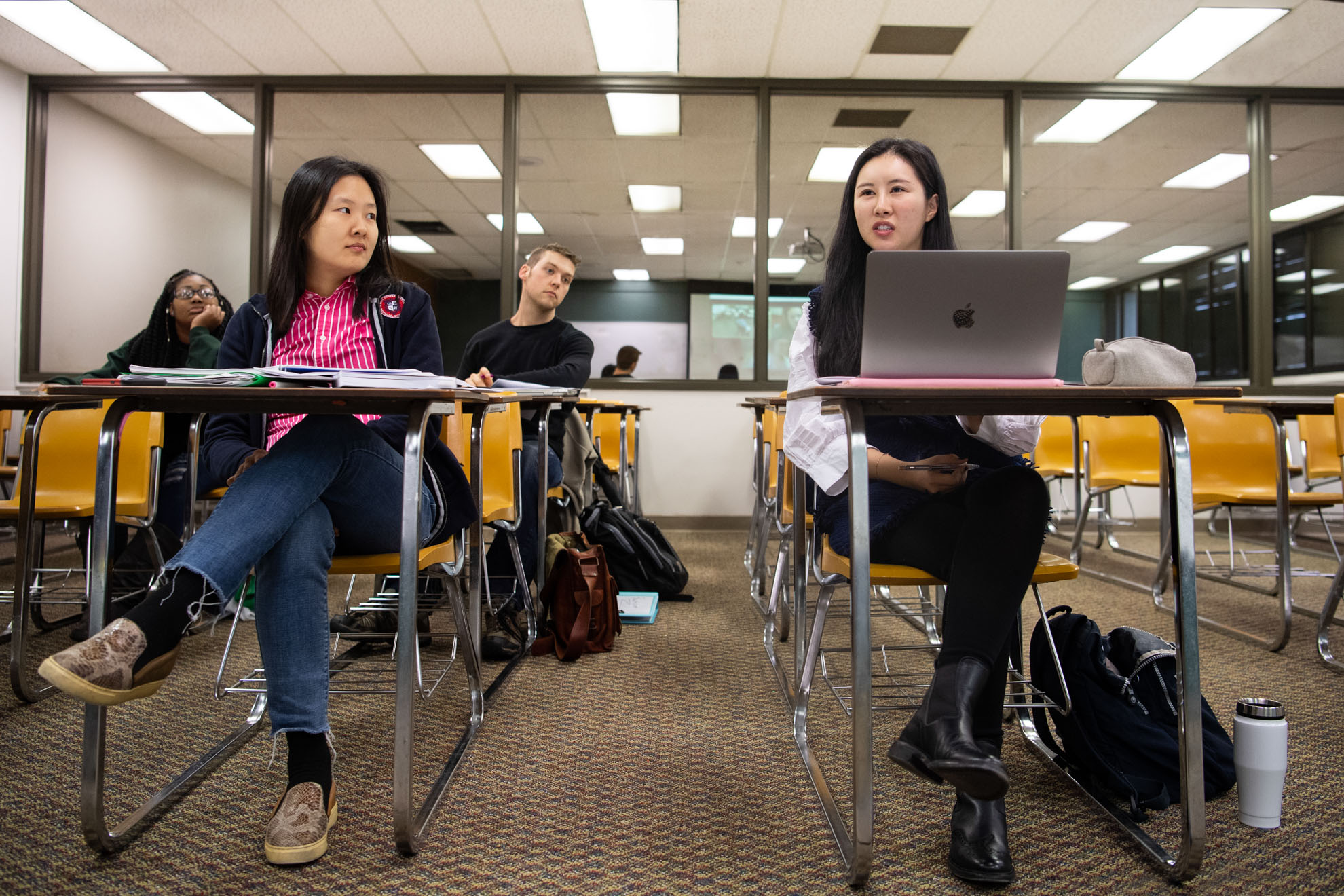 Four students in class with laptops, books, and backpacks.