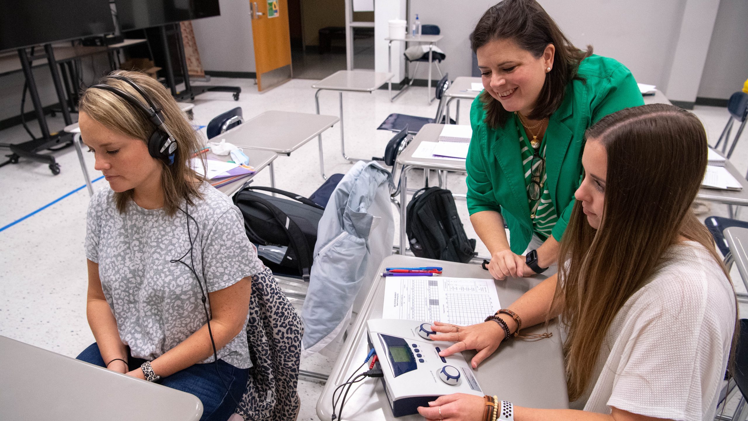 Instructor and student conducting hearing test on another student in a classroom setting.