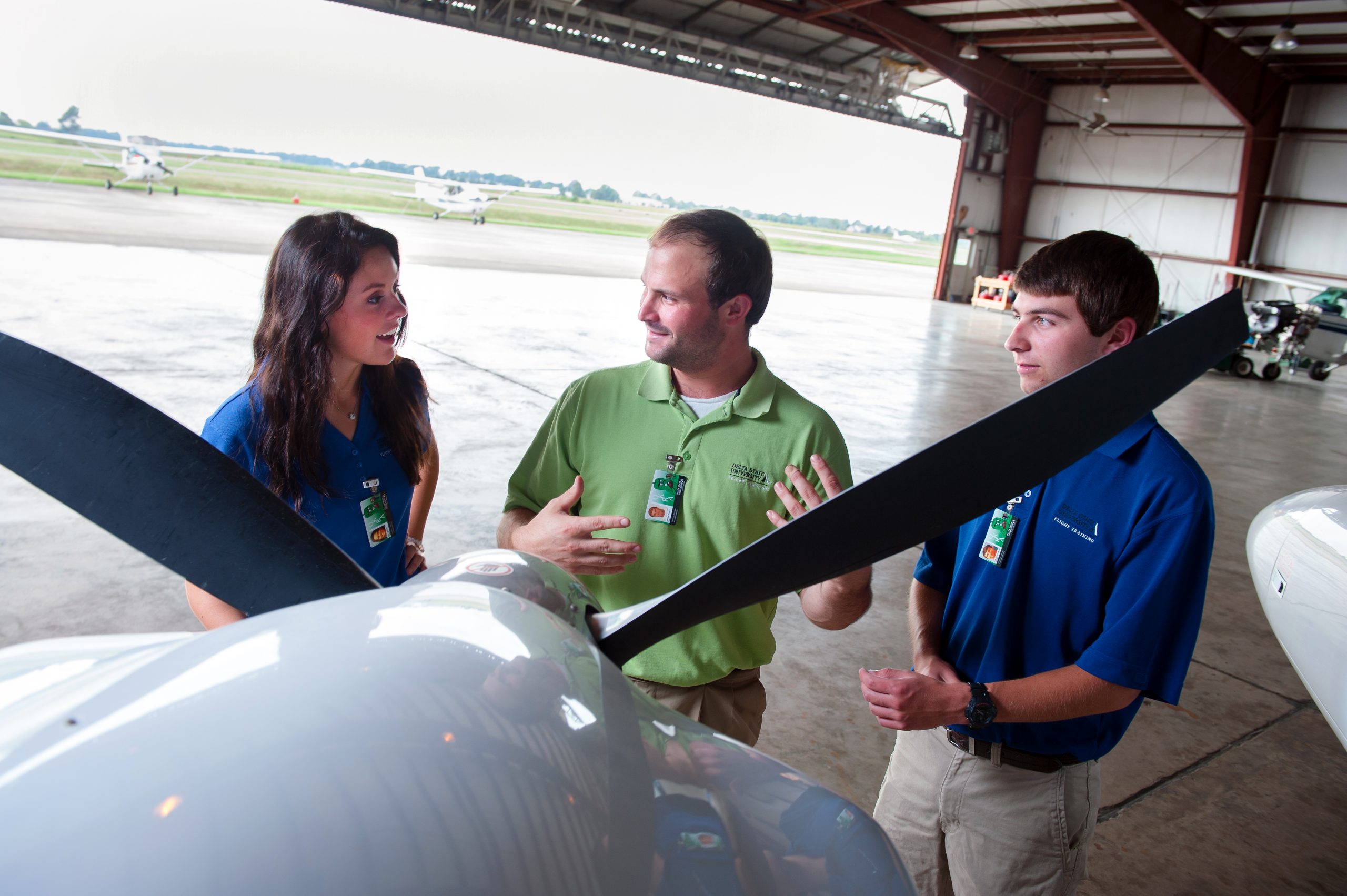 Instructor with two students standing in front of an plane in the airport hanger.