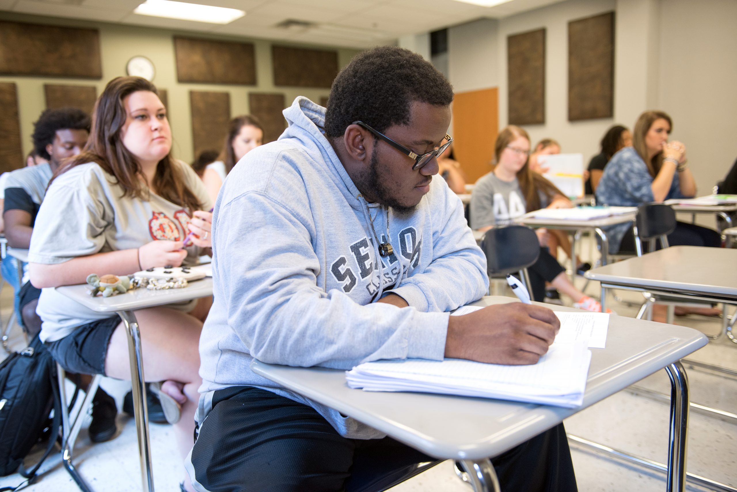 Student in class sitting at a desk, writing in tablet.