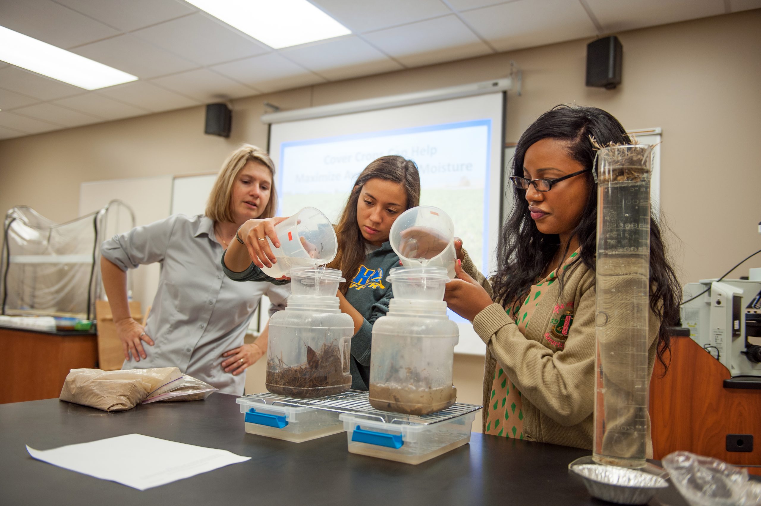 Two students with an instructor conducting a soil and water experiment in class.