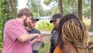 Five students outside with one student showing the others a tree coring tool used to determine the age of trees.