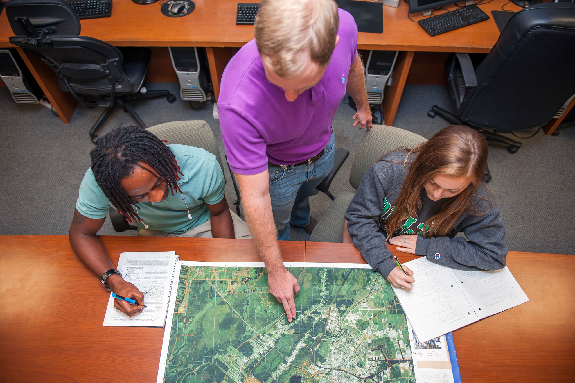 Instructor pointing at map on a table with two students on both sides of him.