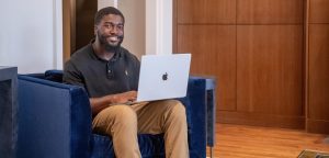 Student sitting in chair in living room with laptop in his lap.