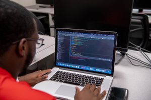 Student writing code on laptop in classroom.