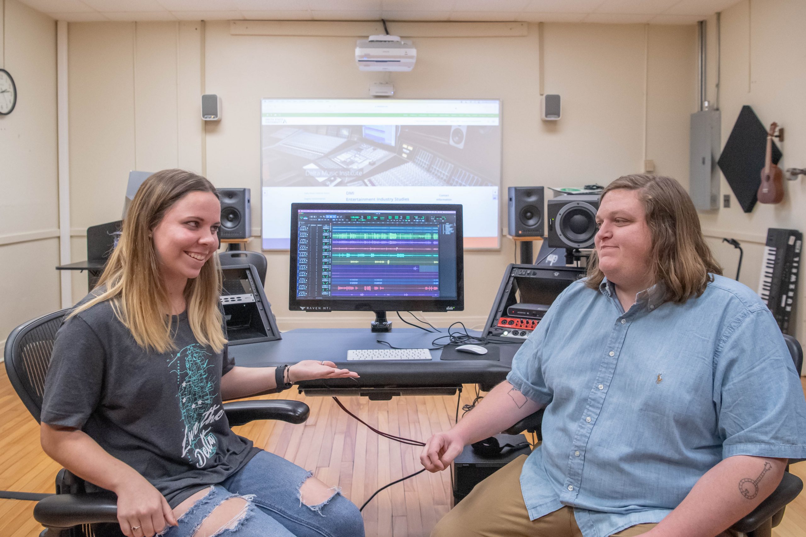 Student and professor sitting next to recording studio equipment.