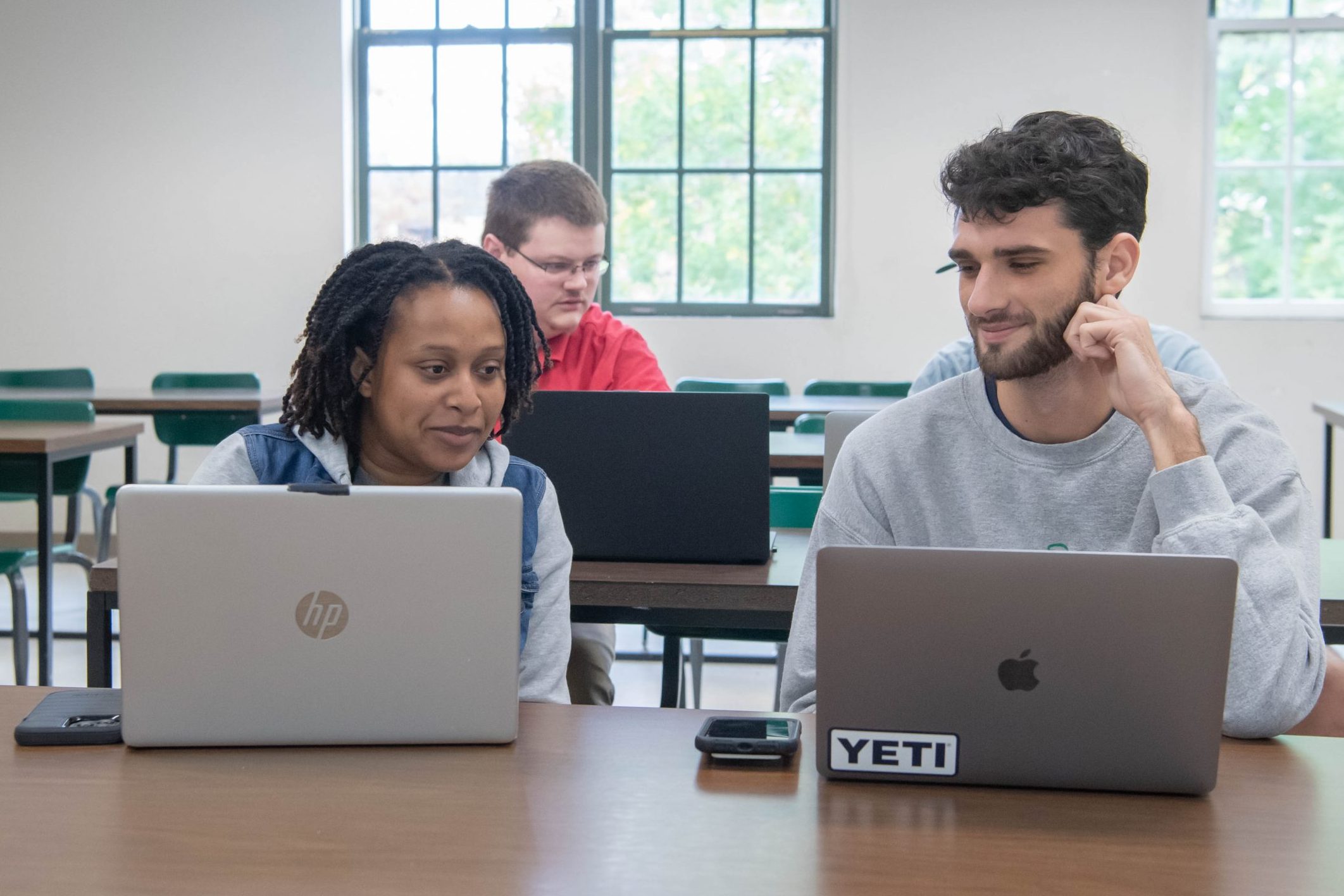 Three students looking at each others laptops in a classroom.