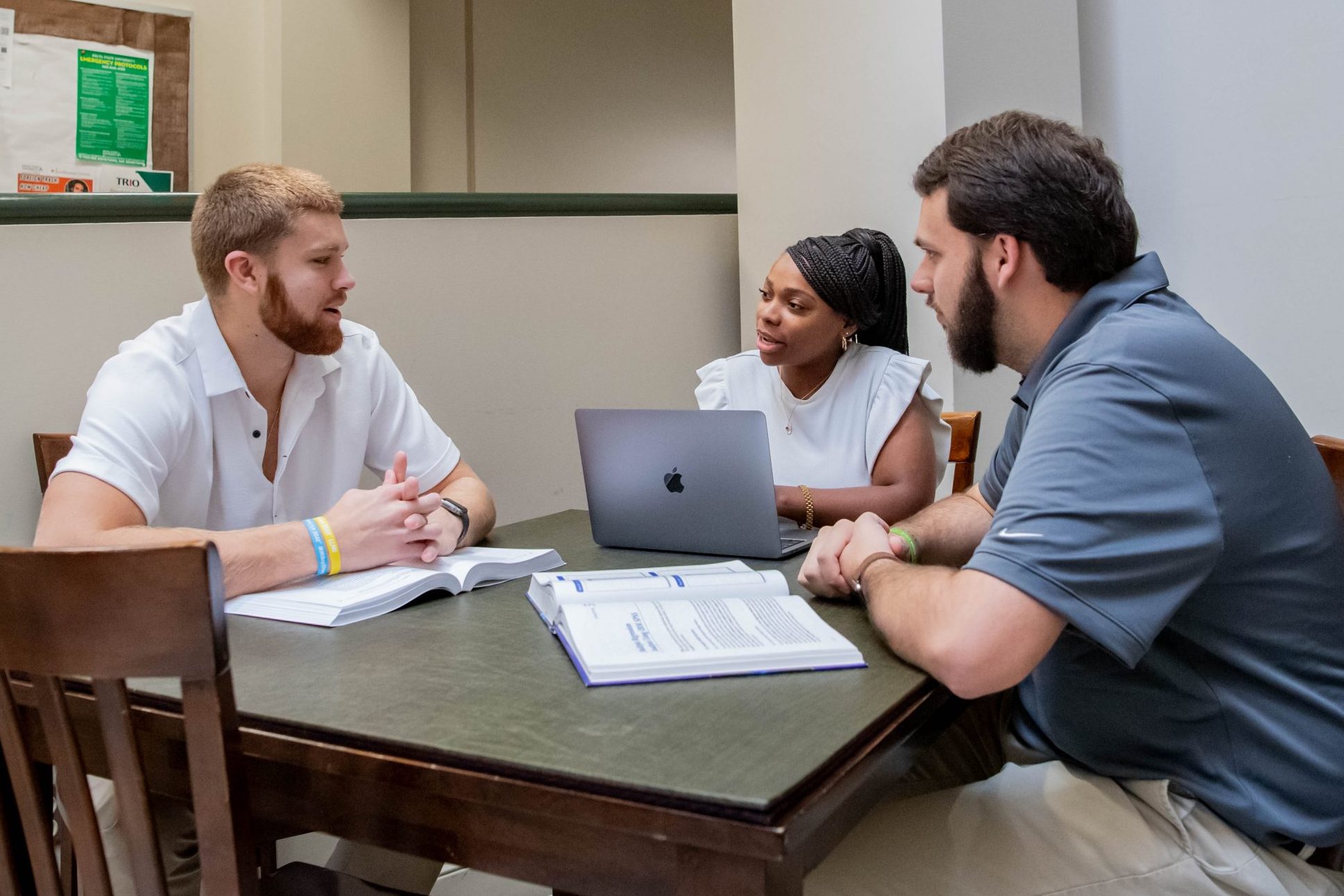 Three students working on assignment together in the College of Business and Aviation lobby, with a laptop and two textbooks.