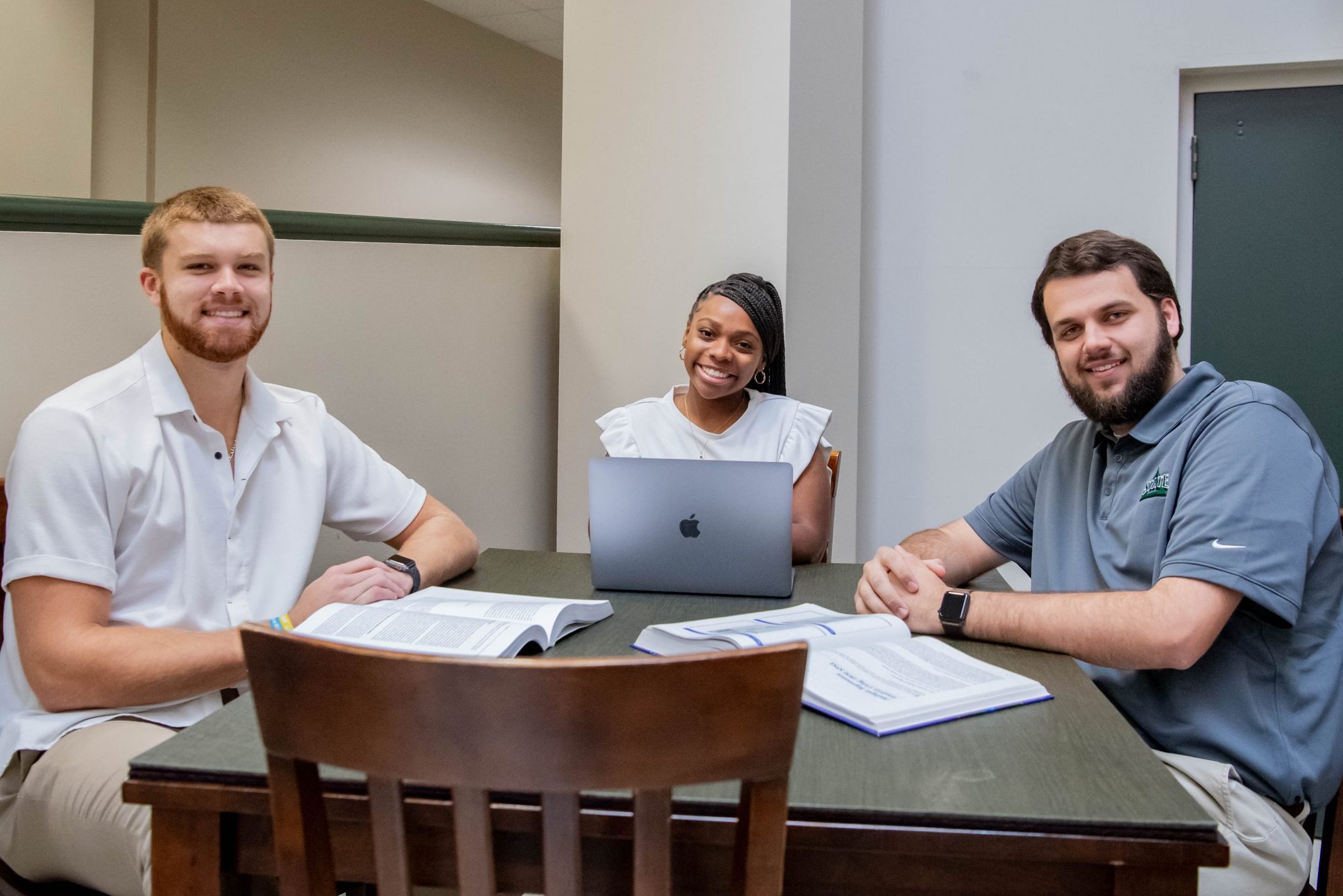 Three students working on assignment together in the College of Business and Aviation lobby, with a laptop and two textbooks.