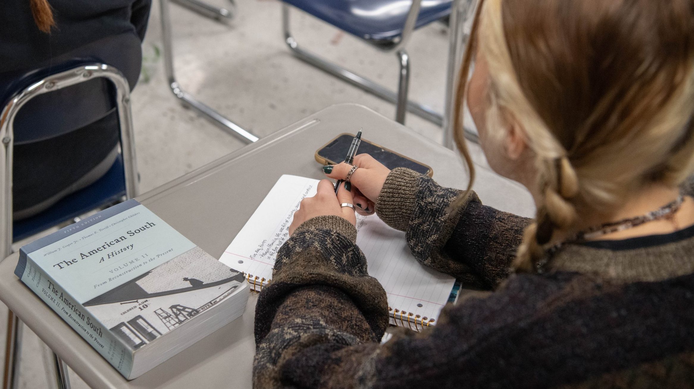 Student sitting at desk with history book, tablet, and phone sitting on the desk.