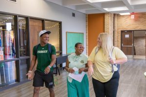 A female leader in education walking with two students on each side of her in the student union. Each of them are smiling.