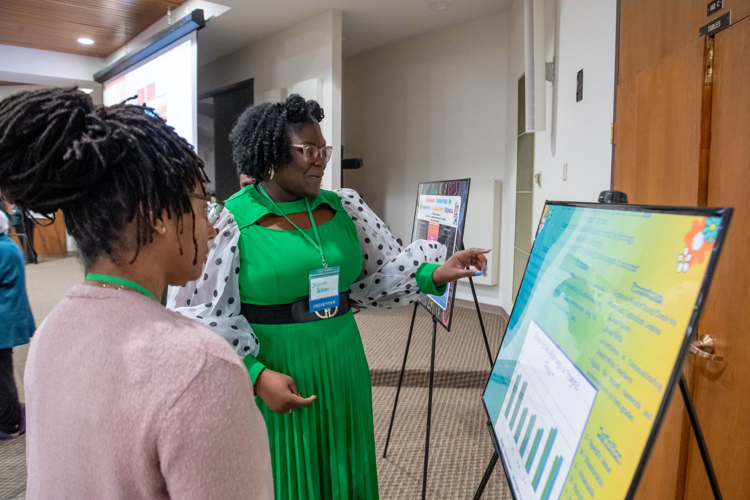 Student presenting research poster information to a person standing next to her.