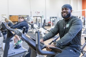 A man on a cycling machine in a fitness center with two other people also on cycling machines behind him.