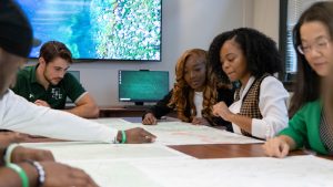 Four students and a professor sitting around a large table, looking at maps.
