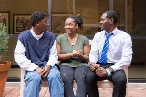 Three African-American students sitting together on a bench outside, engaged in a friendly conversation.