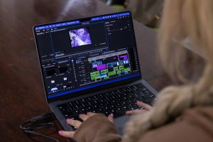 Student working on digital media production, editing video footage with professional software on a laptop.
