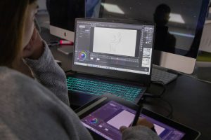 Arts entrepreneurship student creating digital artwork on a tablet while using design and animation software on a laptop in a computer lab.