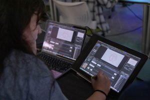 Arts entrepreneurship student working on digital illustration, drawing with a tablet while using design software on a laptop.