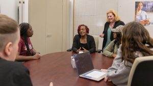 Instructor leading a discussion with students seated around a table in a classroom.