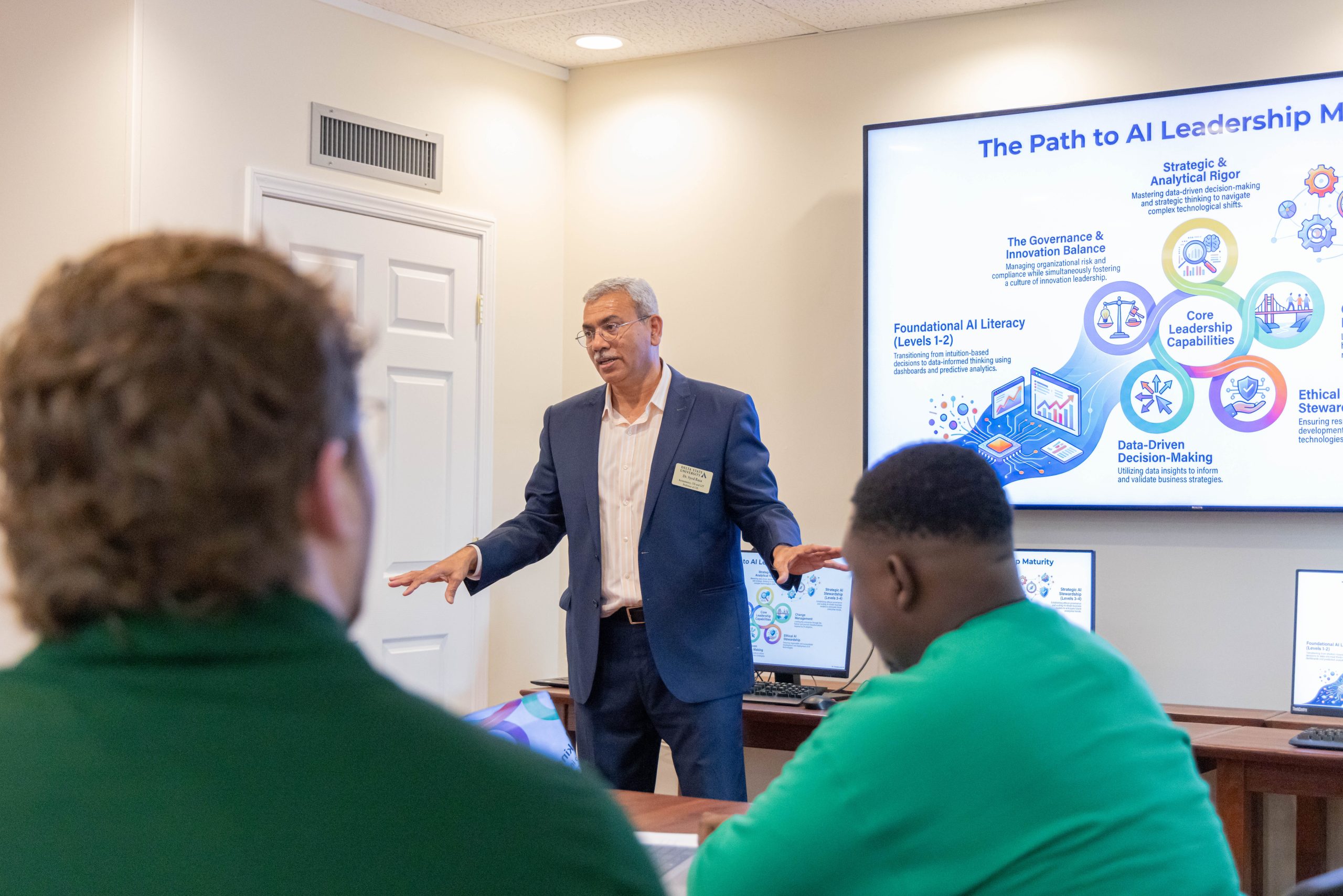 Instructor presenting AI leadership concepts to students in a classroom, with a screen displaying "The Path to AI Leadership" during a lecture.