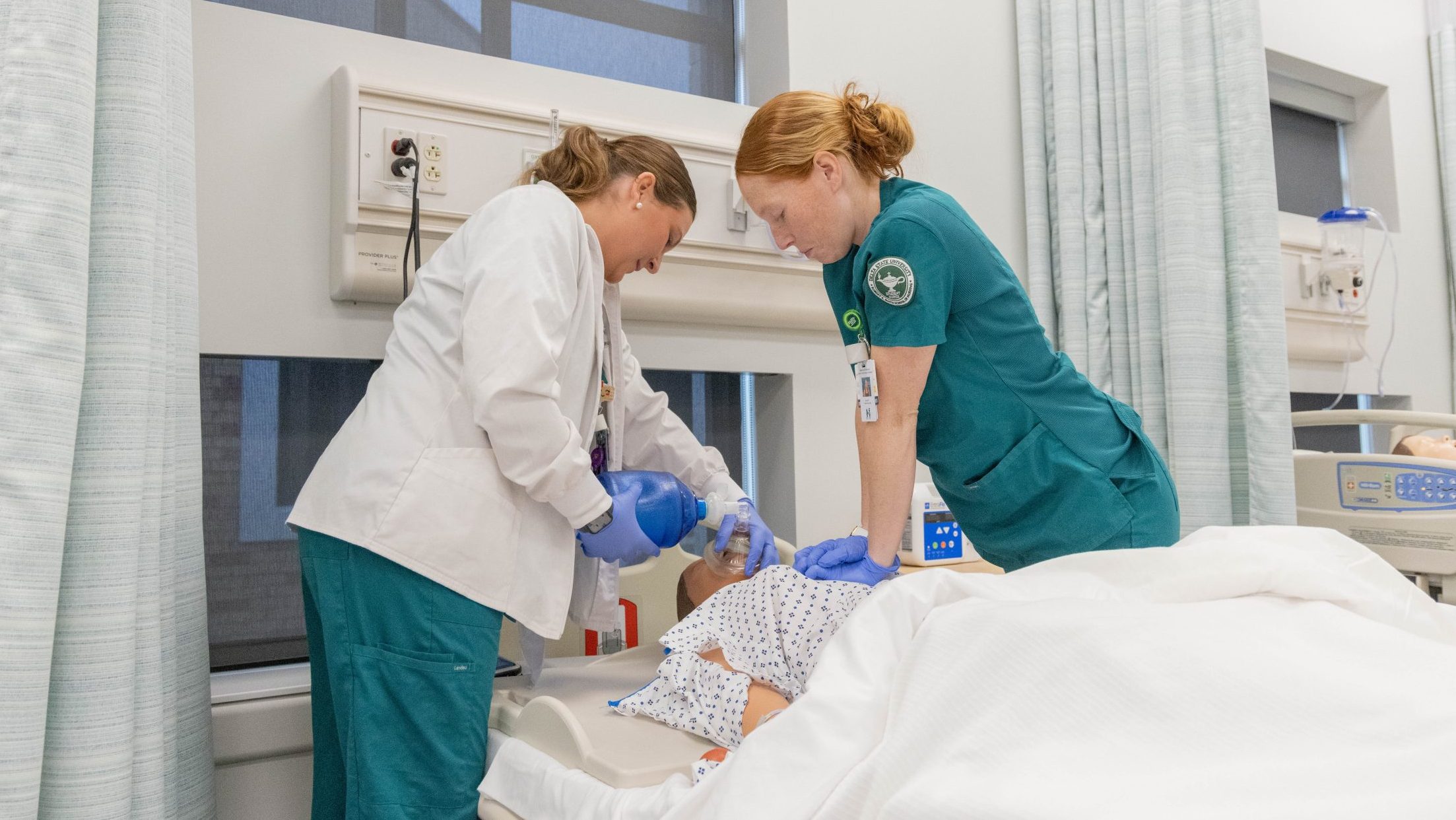 Nursing students practicing bedside patient care in a healthcare simulation lab.