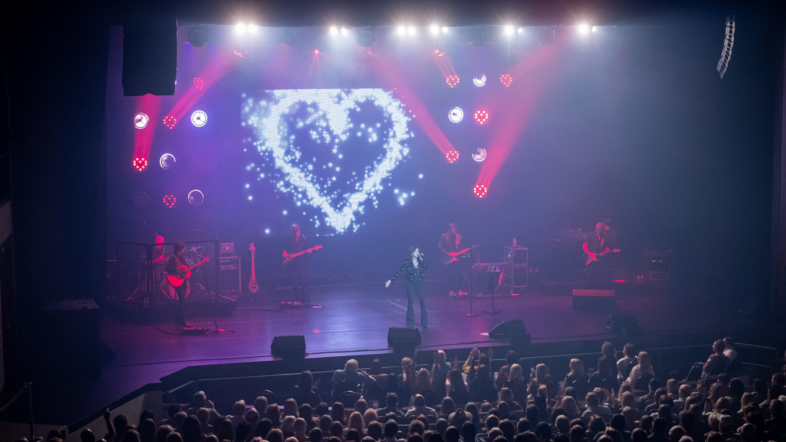 A band performing at a live concert with lights and large crowd at Bologna Performing Arts Center.