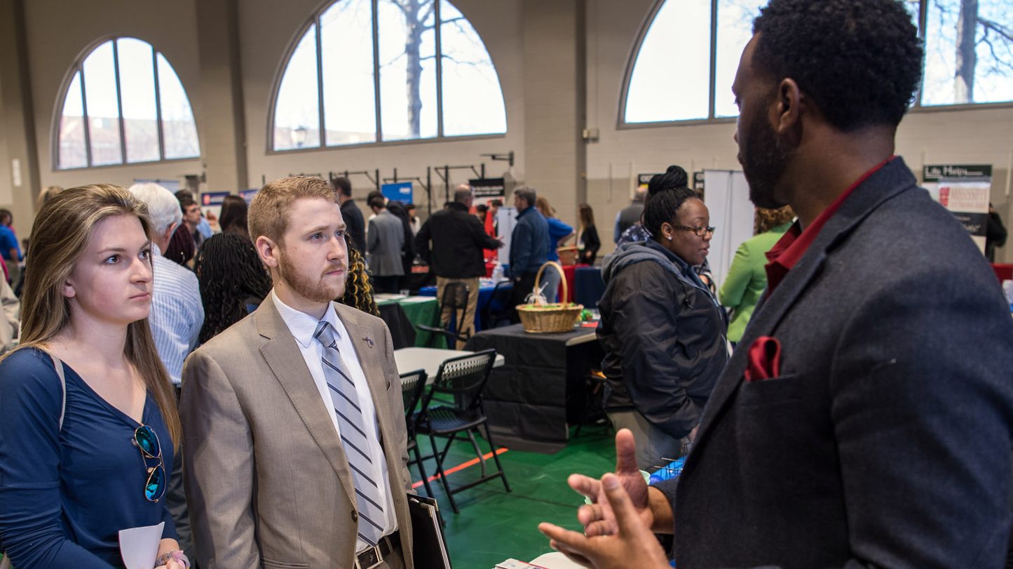 Two students at a career fair, speaking with a potential employer.