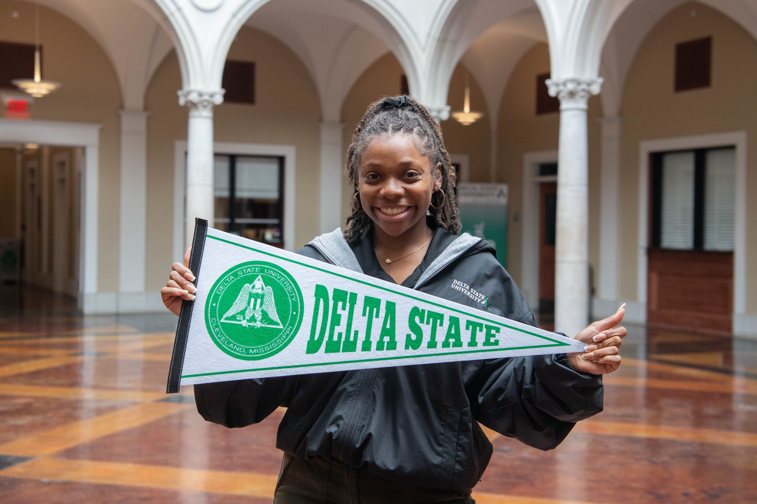 Admissions recruiter holding Delta State pennant in the administration building.