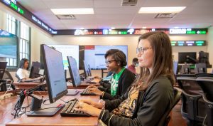 Students analyzing data on computers in a business lab with live stock ticker displays.
