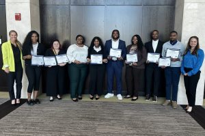Group of students posing with certificate at a college recognition ceremony, flanked by two faculty members.