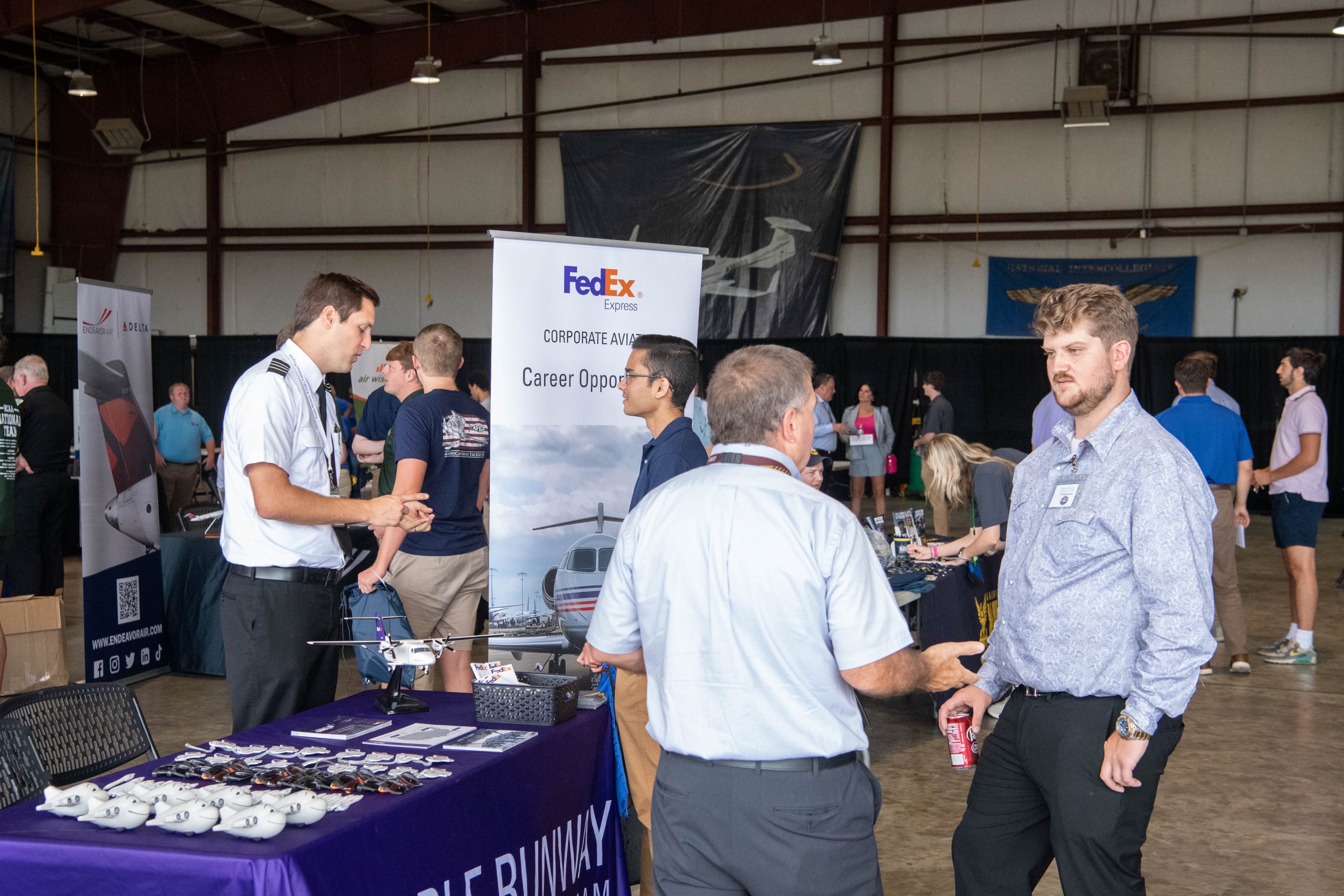 Aviation students interacting with company representatives at a career fair event in an aircraft hanger.