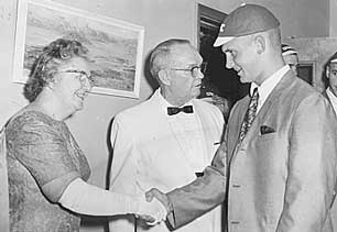 A freshman sporting a shaved head and a green beanie greets President Ewing and his wife