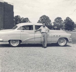 Man posing in front of car, B&W.