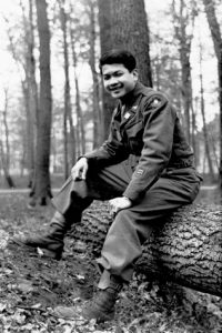 James Lum in uniform, sitting on log, B&W