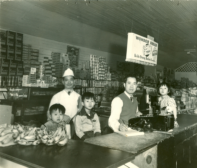 Family poses behind counter. B&W.