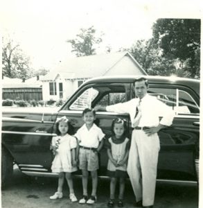 Man and three children pose in front of car, B&W.
