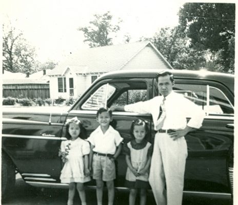 Man and three children pose in front of car, B&W.