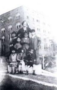 Woman posing with children outside building. B&W.