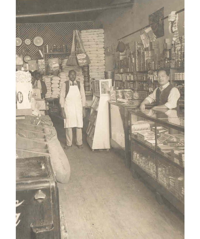 Three men, one of whom is behind a counter, in a grocery.
