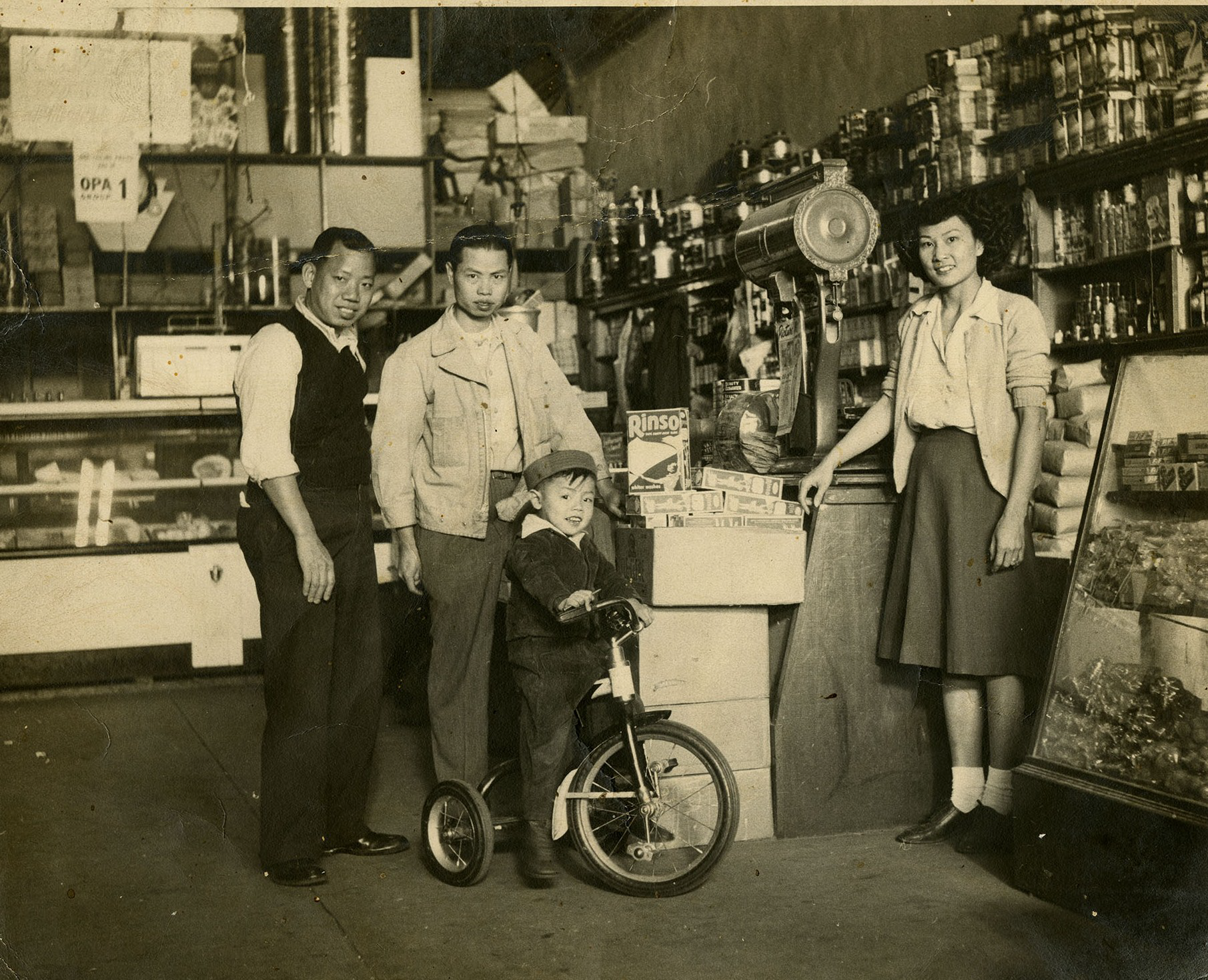 Two men, one little boy with a bike, and a young woman stand in front of a counter.