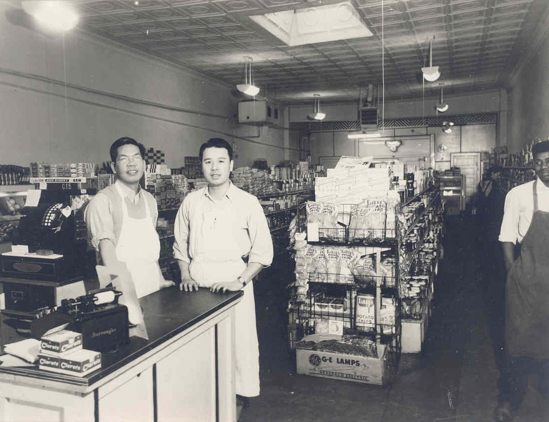 Two grocery store owners stand together in a grocery store.