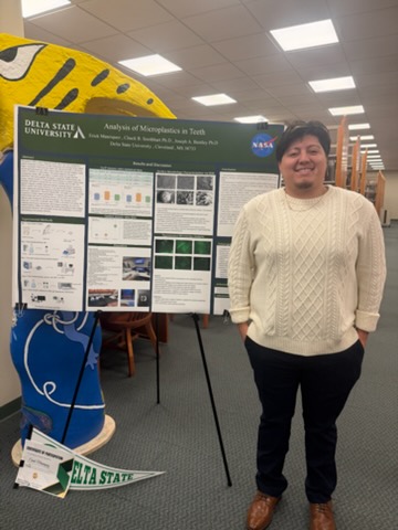 Erick Manriquez stands next to his research poster at the Academic Research Showcase.