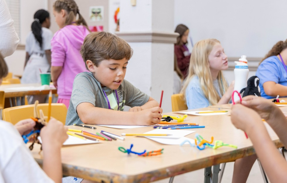 a young boy sitting at a desk doing arts and crafts